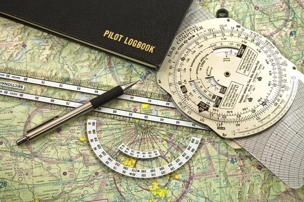 Top view of a map with a pilot logbook, pen, ruler, and protactors on top of it